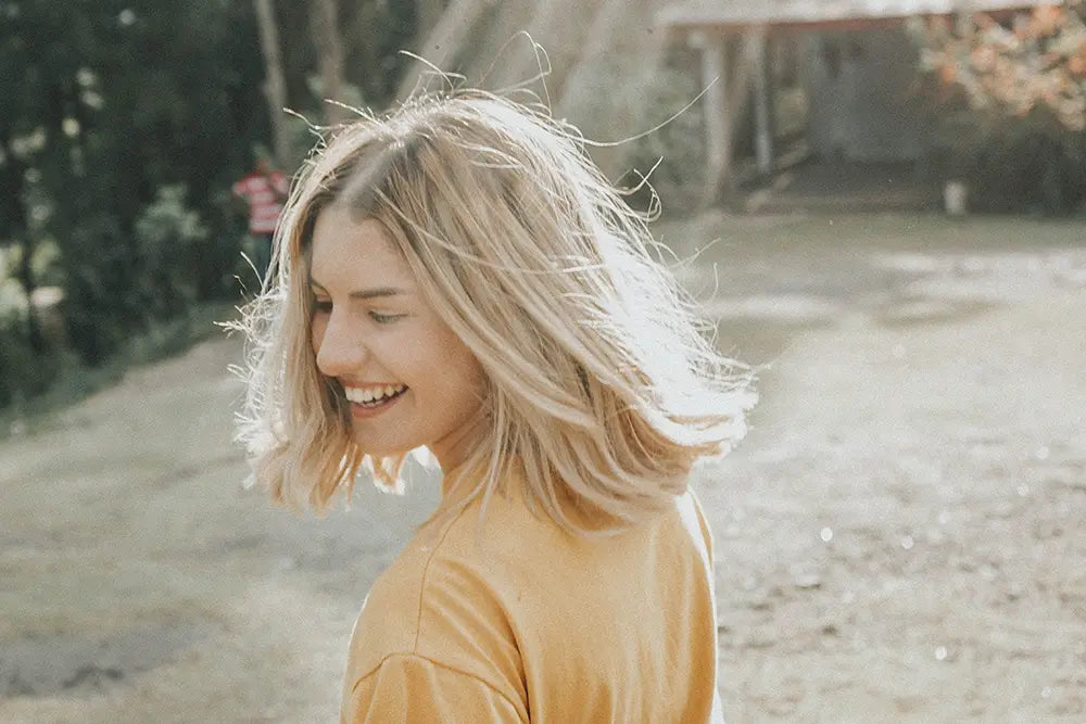 femme blonde tshirt jaune cheveux mi longs en exterieur rayon de soleil vitamines contre la fatigue